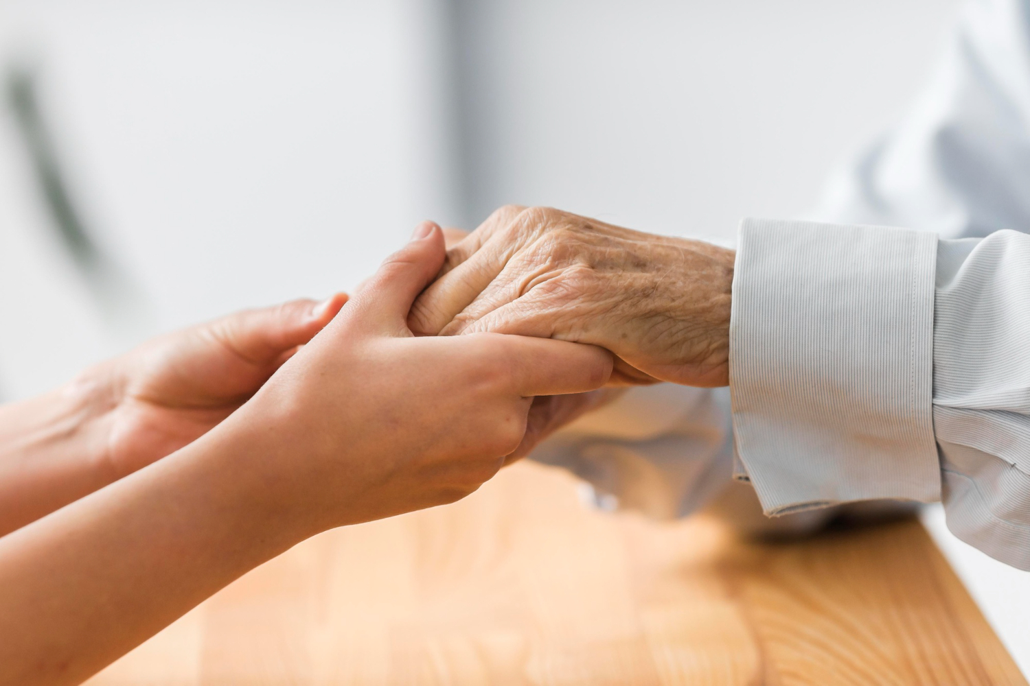 A caregiver holding an older adult’s hand — the dignity this work is built on