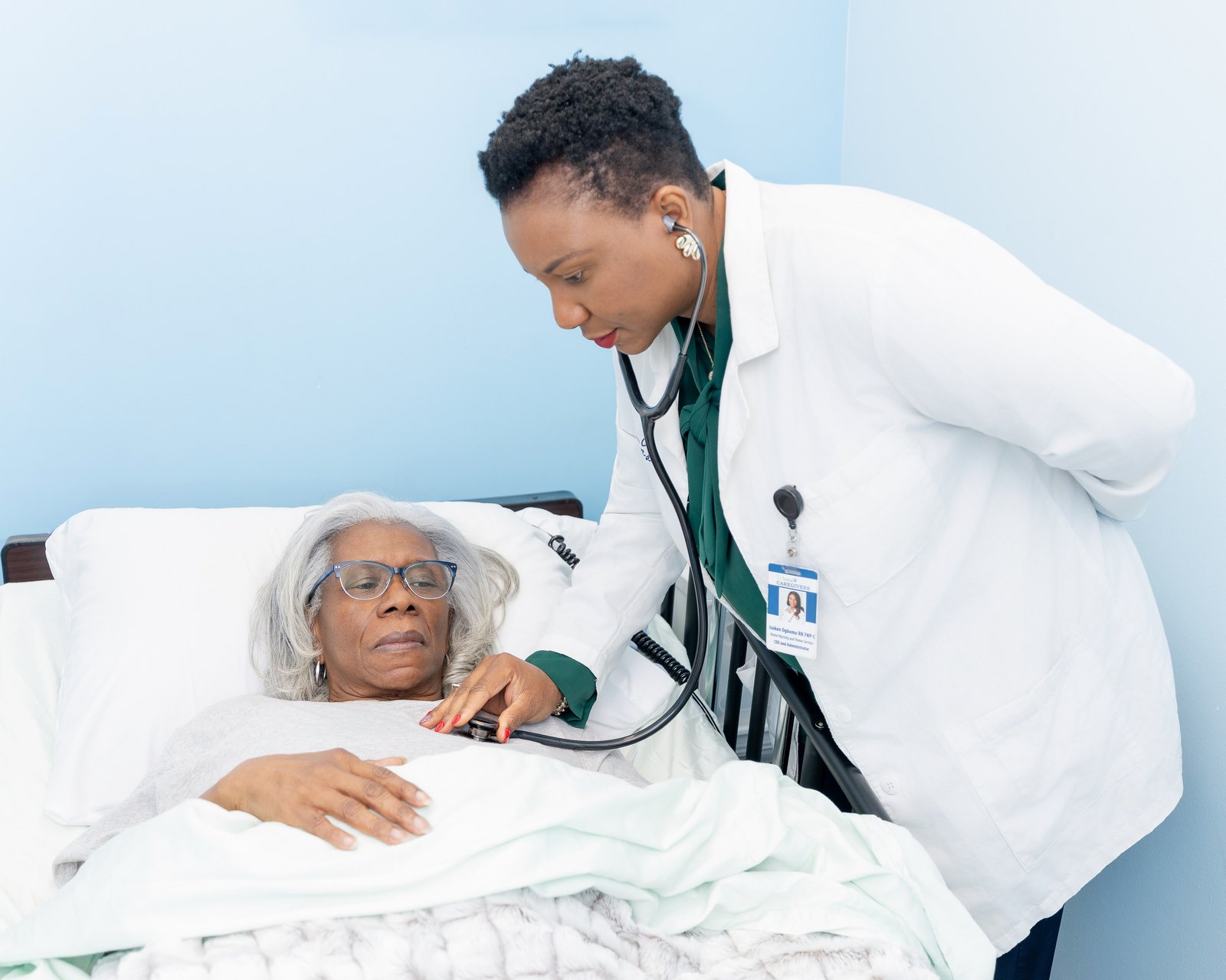 Isoken Ogbomo listening to a client’s chest with a stethoscope at the bedside