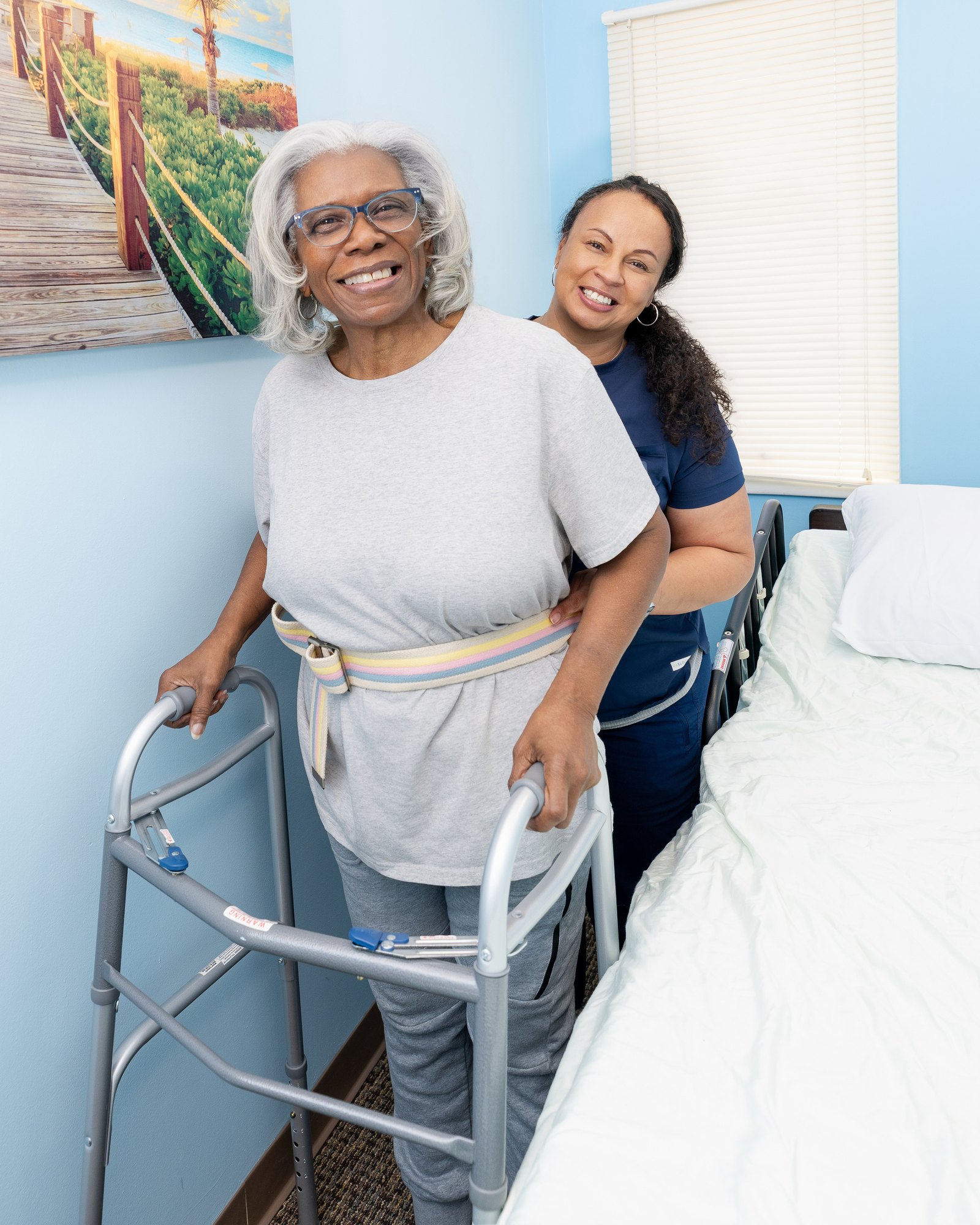 A Care Partner supporting an older woman as she stands with a walker