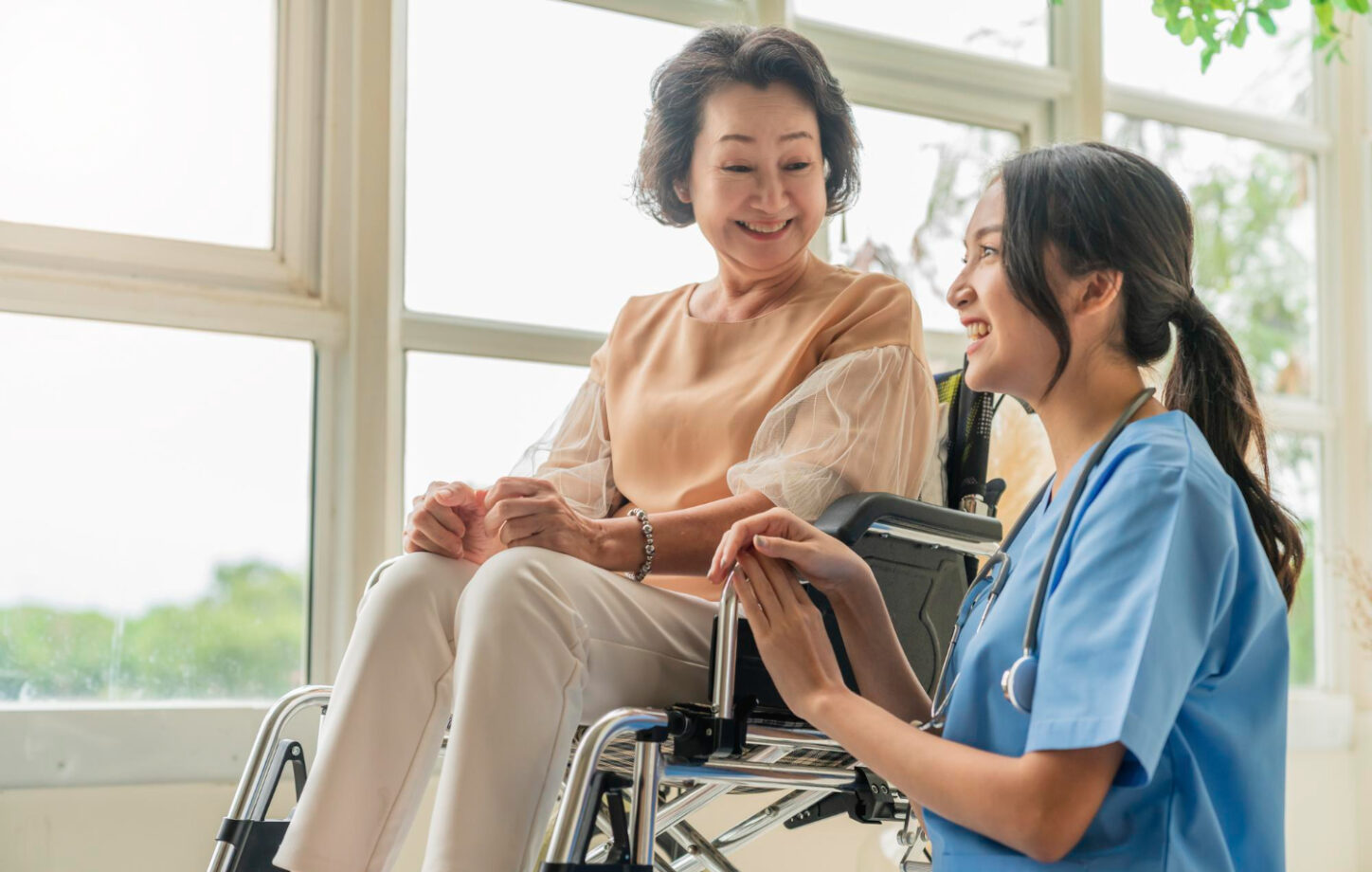 A nurse speaking with an older woman seated in a wheelchair