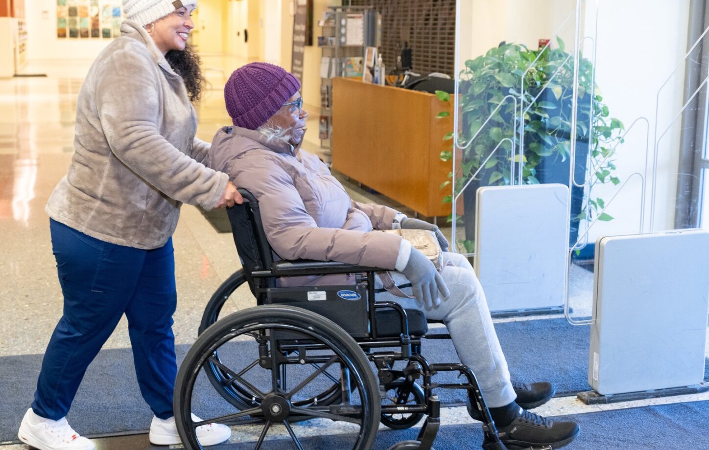 A Care Partner walking with a client using a wheelchair in a bright lobby